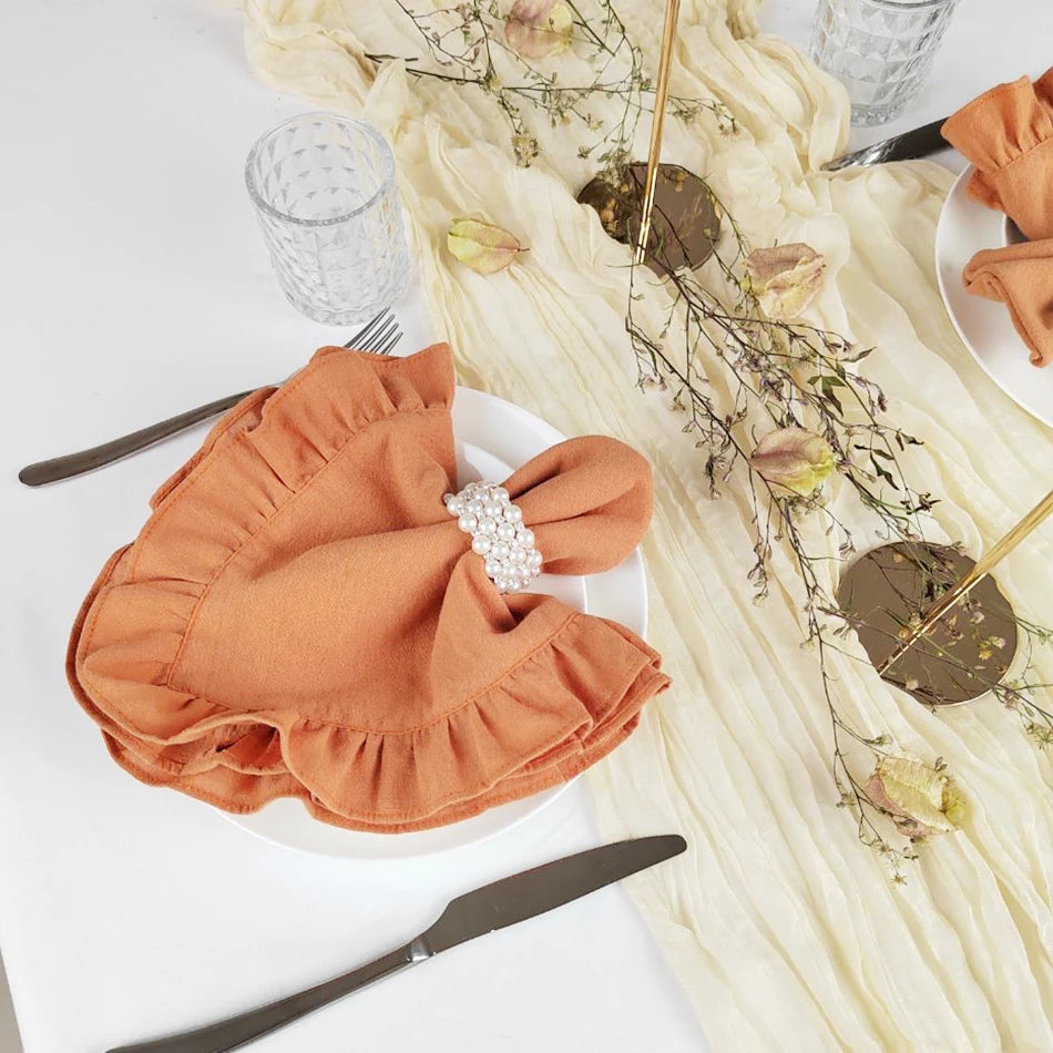 Cette image met en scène une composition élégante avec des accessoires de table, notamment un noeud en tissu orange posé sur une assiette blanche, accompagné de fleurs et de branches feuillues disposées avec soin.