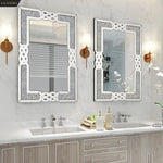 Deux miroirs muraux élégants aux cadres argentés ornés de motifs entrelacés, reflétant une salle de bain avec un meuble-lavabo en bois nuancé et des accessoires assortis, créant une ambiance raffinée et harmonieuse.