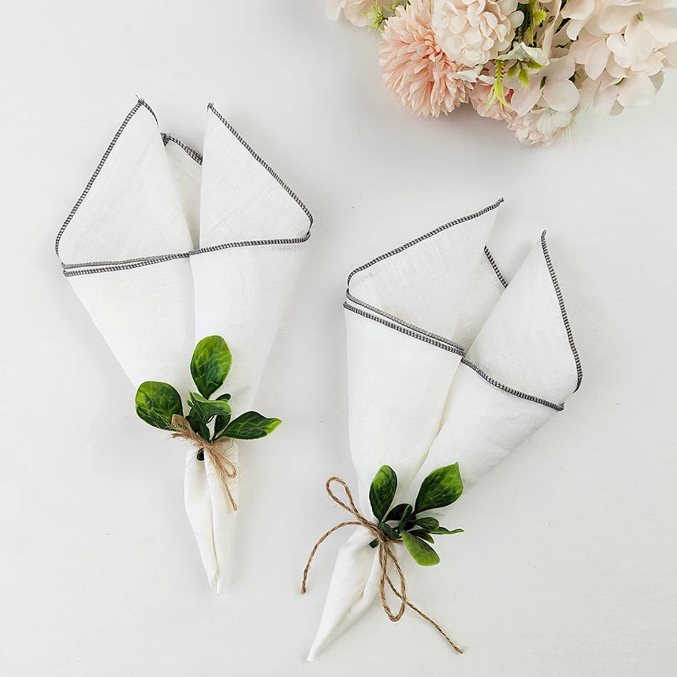 Serviettes de table blanches décorées de feuilles de verdure, liées avec de la ficelle de jute, entourées d'un bouquet de fleurs roses délicates sur fond blanc.