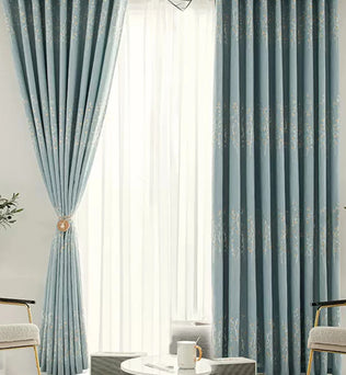 Rideaux occultants bleus à motifs floraux installés dans un salon lumineux avec voilage blanc.