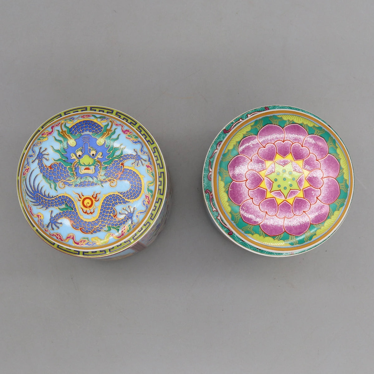 Deux boîtes colorées ornées de motifs traditionnels orientaux, l'une montrant un dragon bleu enroulé, l'autre une fleur rose épanouie, représentant une riche tradition décorative.