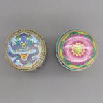 Deux boîtes colorées ornées de motifs traditionnels orientaux, l'une montrant un dragon bleu enroulé, l'autre une fleur rose épanouie, représentant une riche tradition décorative.