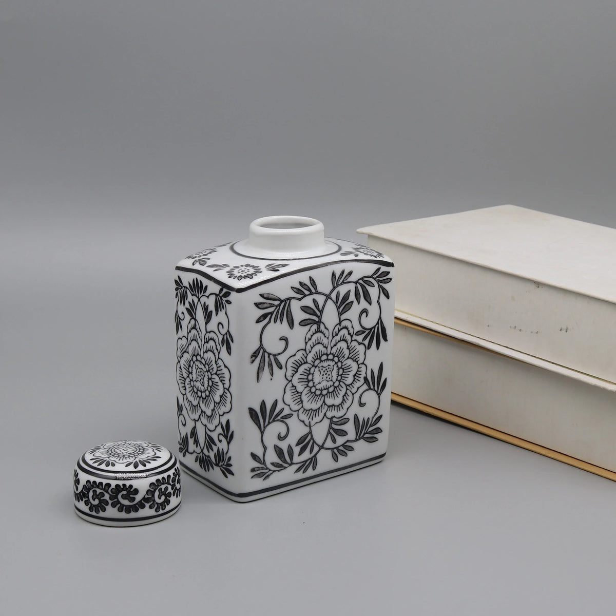 Contenant orné de motifs floraux noirs et blancs, avec un couvercle assorti, posé à côté de quelques livres.