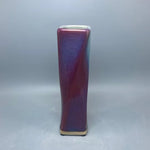 Vase en céramique de couleur pourpre brillante avec une forme élancée et élégante.