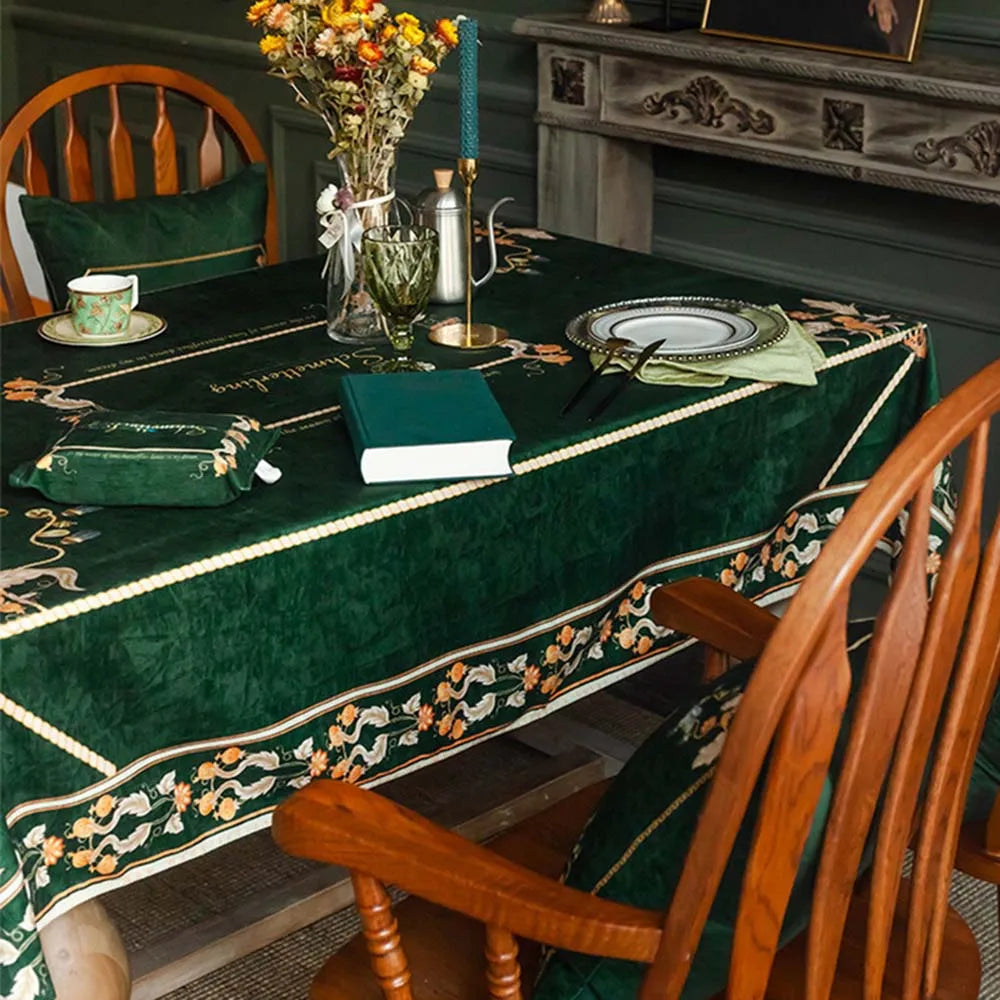 Une table couverte d'un élégant linge de table vert décoré de fleurs, avec un arrangement floral, une vaisselle et des livres, créant une ambiance chaleureuse et confortable.