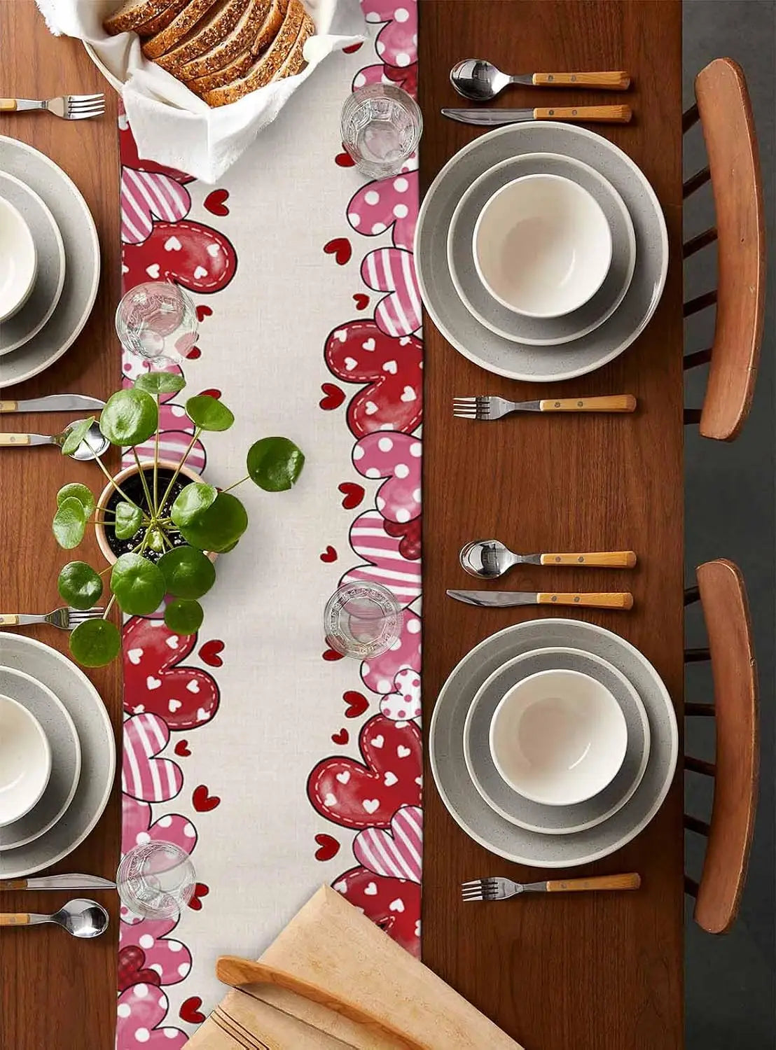 Une table dressée avec de la vaisselle et des couverts sur un joli motif de cœurs et de pois, avec un plat de pain et une plante verte.