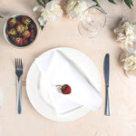 Assiette blanche avec une seule fraise fraîche posée sur une serviette, entourée de pâquerettes blanches et d'un verre en cristal sur un fond beige.