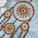 Des attrape-rêves en macramé marron ornés de perles et de perles en bois sont disposés sur une surface grise.