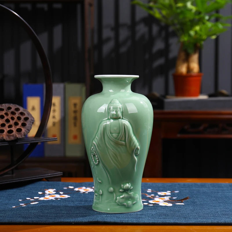 Vase en céramique vert menthe orné d'une statuette bouddhiste, posé sur une table de bois avec des éléments décoratifs.
