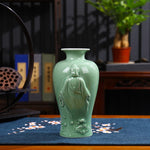 Vase en céramique vert menthe orné d'une statuette bouddhiste, posé sur une table de bois avec des éléments décoratifs.