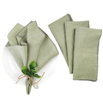Serviettes en lin vert pastel et feuilles de menthe liées par un cordon, sur fond blanc.