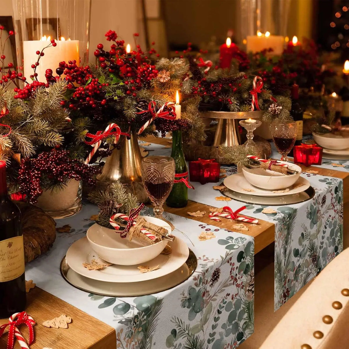 Une table décorée avec des bougies allumées, des branchages de sapin, des boules rouges et des bonbons de Noël, créant une ambiance festive et chaleureuse.