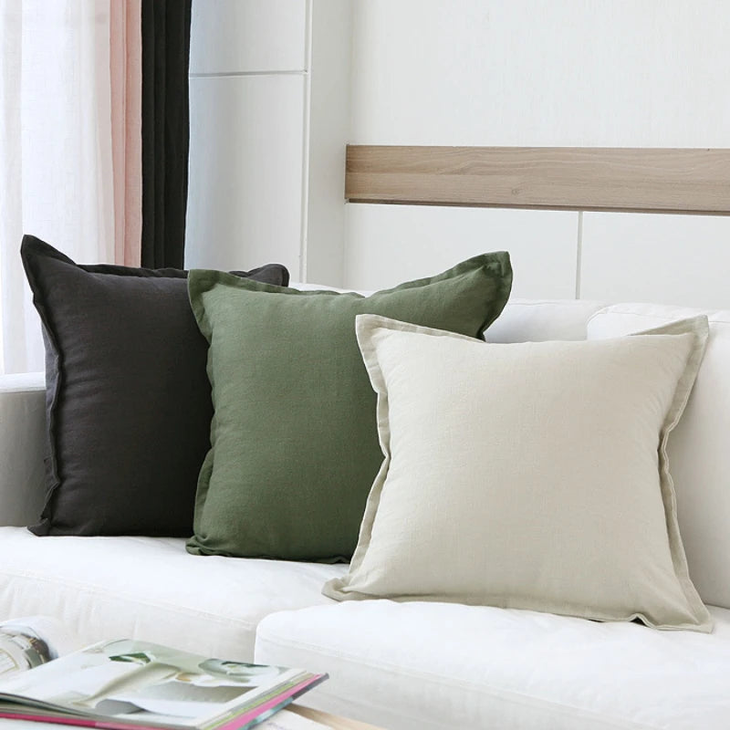 Des coussins de couleurs vert olive et blanc, sur un canapé blanc dans une chambre aux murs et rideaux légers, créant une ambiance apaisante et harmonieuse.