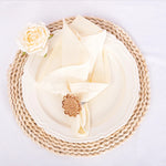 Une délicate serviette blanche ornée d'une rose et d'un jonc tressé, créant une mise en scène élégante et épurée.