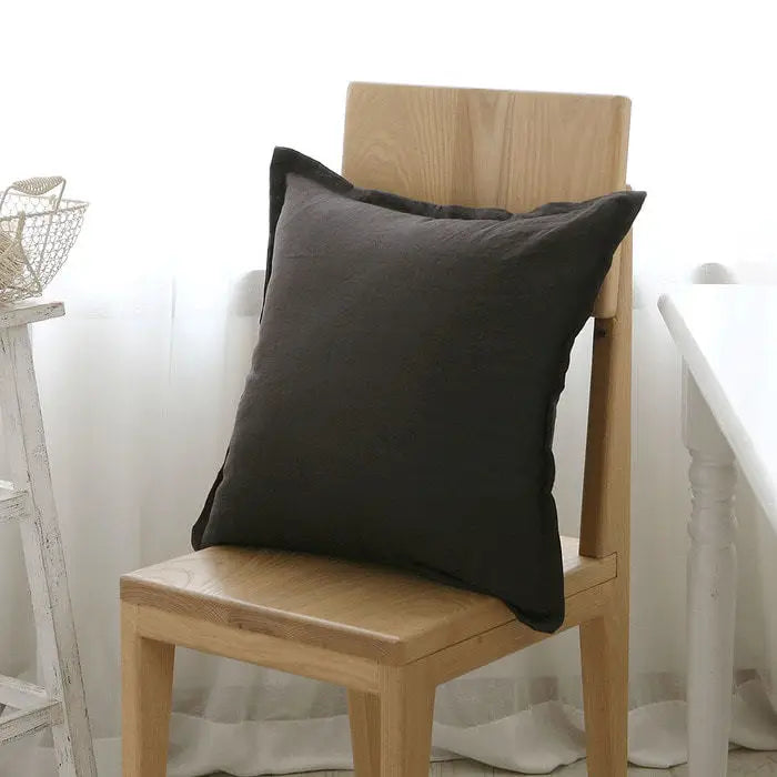 Coussin décoratif noir sur une chaise en bois dans un intérieur moderne et épuré.