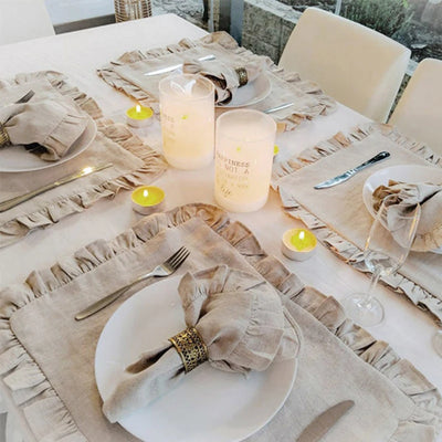 Une table élégamment dressée avec des serviettes beiges chiffonnées, des bougies allumées et des ustensiles de table soigneusement disposés, créant une ambiance chaleureuse et invitante.