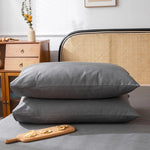 Deux oreillers gris posés sur un lit en bois, avec des meubles et un bouquet de fleurs dans la pièce.