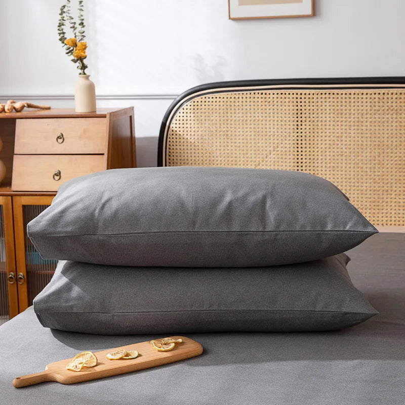 Deux oreillers gris posés sur un lit en bois, avec des meubles et un bouquet de fleurs dans la pièce.