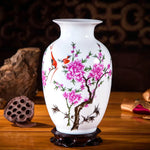 Une élégante poterie blanche ornée de fleurs de pivoines roses et de petits oiseaux rouges, sur un socle en bois sombre, dégageant une atmosphère traditionnelle et raffinée.