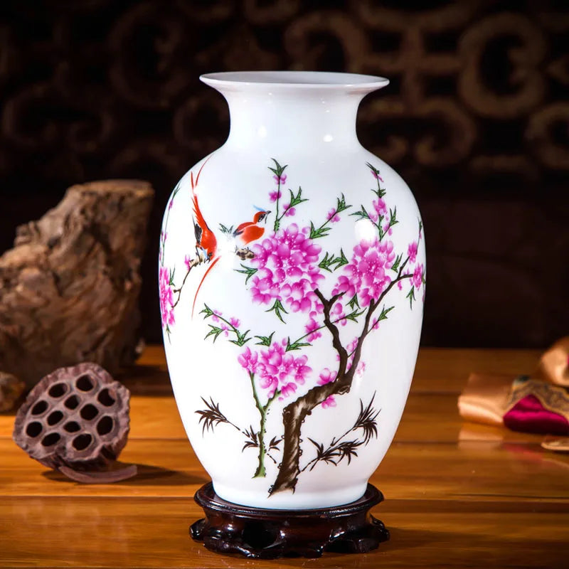 Un vase en porcelaine blanche décoré de fleurs de cerisier roses épanouies et d'oiseaux rouges sur un socle en bois sombre.