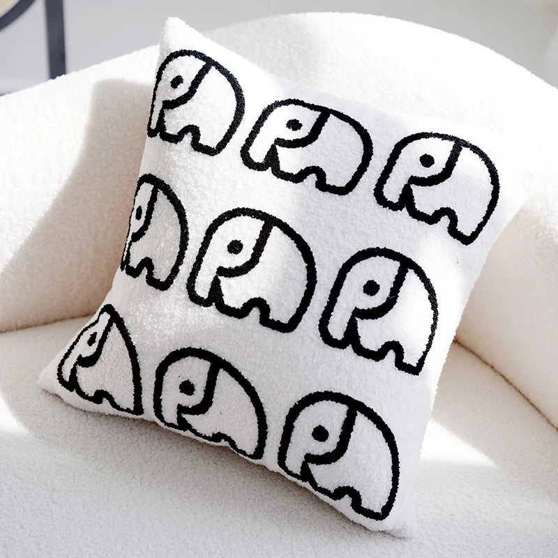 Coussin décoratif blanc avec motif éléphants noirs stylisés.