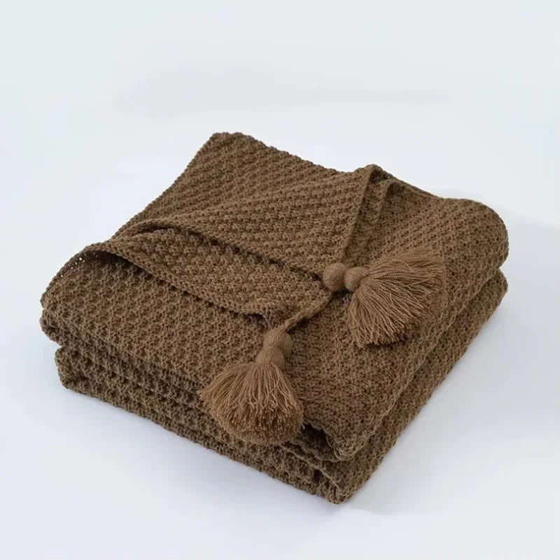 Couverture en tricot brun doux avec des glands décoratifs, idéale pour se réchauffer et apporter une touche cocooning à l'intérieur.