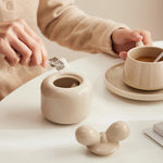 Une tasse de café et une théière en céramique blanche posées sur une table.