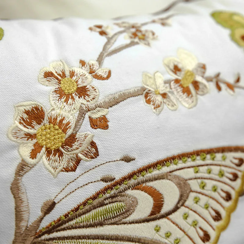Un gros plan de motifs floraux brodés avec des couleurs chaudes sur un tissu blanc.