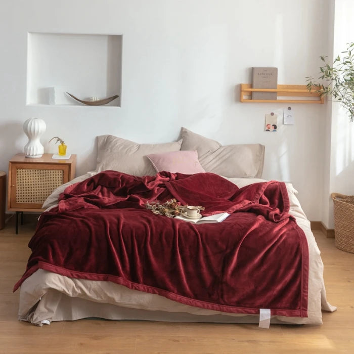 Chambre confortable avec lit douillet, couverture en velours rouge et décoration minimaliste, étagère en bois et détails charmants.