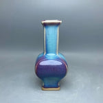 Vase en céramique de couleur bleue et violette, avec une forme arrondie et un long col étroit.