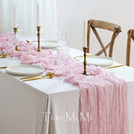 Une table élégante décorée de chandelles dorées, de vaisselle fine et d'une nappe rose aux franges soyeuses, créant une atmosphère romantique et raffinée.