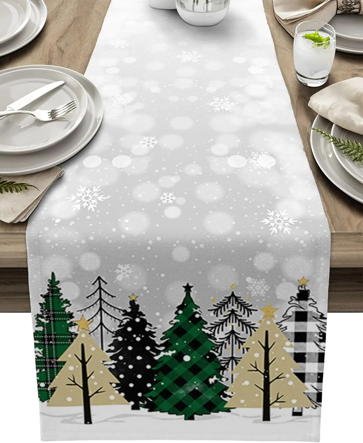 Cette image montre une nappe de table en tissu avec un motif hivernal de sapins de Noël et de flocons de neige sur un fond gris clair, créant une ambiance festive et cosy pour la décoration de table.