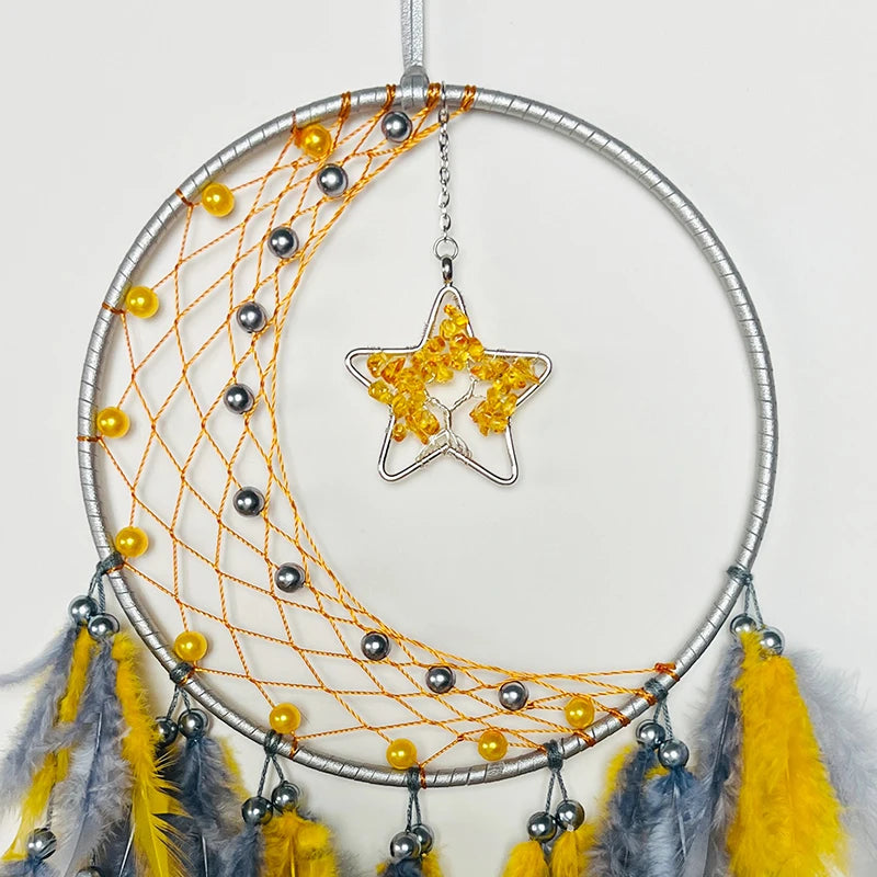 Un magnifique attrape-rêves argenté et jaune suspendu par des chaînettes, décoré d'étoiles en ambre et de plumes jaunes et grises.
