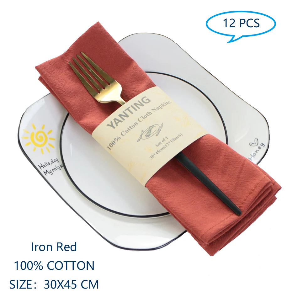 Des serviettes de table en coton rouges, pliées avec une fourchure dorée, posées sur des assiettes blanches avec le logo du jour bonjour au fond.