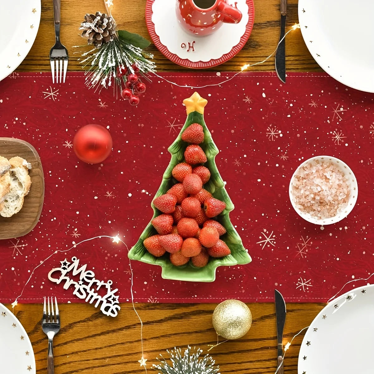 Une décoration de table de Noël avec un arbre de Noël en fraises, des boules de Noël rouges et dorées, et des éléments décoratifs sur un fond rouge pailleté.