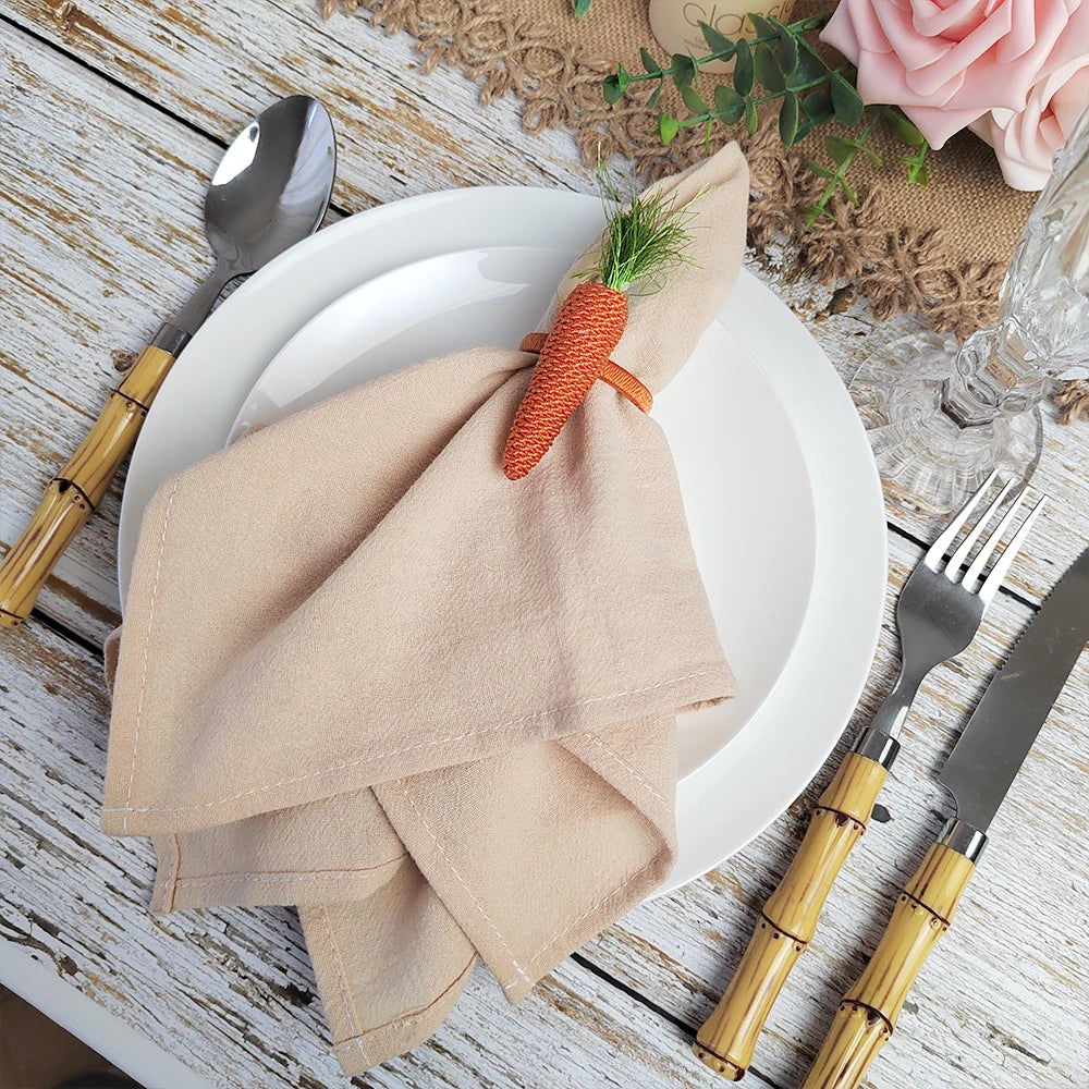 Sur une table en bois, une assiette blanche est entourée de serviettes beige, d'un couvert doré et d'un bouquet de roses roses, créant une atmosphère élégante et raffinée pour un repas.
