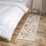Petit tapis en coton orné de fleurs et de motifs géométriques, posé au pied d'un lit douillet aux draps immaculés.