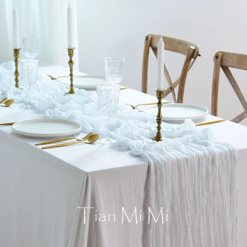 Une table dressée avec élégance, comprenant des assiettes blanches, des verres et des chandeliers dorés sur un linge de table blanc froissé, évoquant une atmosphère raffinée et sophistiquée.