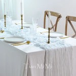 Une table dressée avec élégance, comprenant des assiettes blanches, des verres et des chandeliers dorés sur un linge de table blanc froissé, évoquant une atmosphère raffinée et sophistiquée.