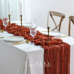 Une élégante table de salle à manger avec une nappe blanche et une décoration de couleur rouille, comprenant des chandeliers, des verres cristallins et une nappe texturée.