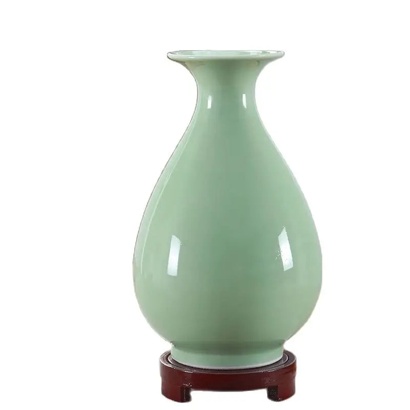 Magnifique vase en céramique de couleur vert pâle posé sur un support en bois foncé.