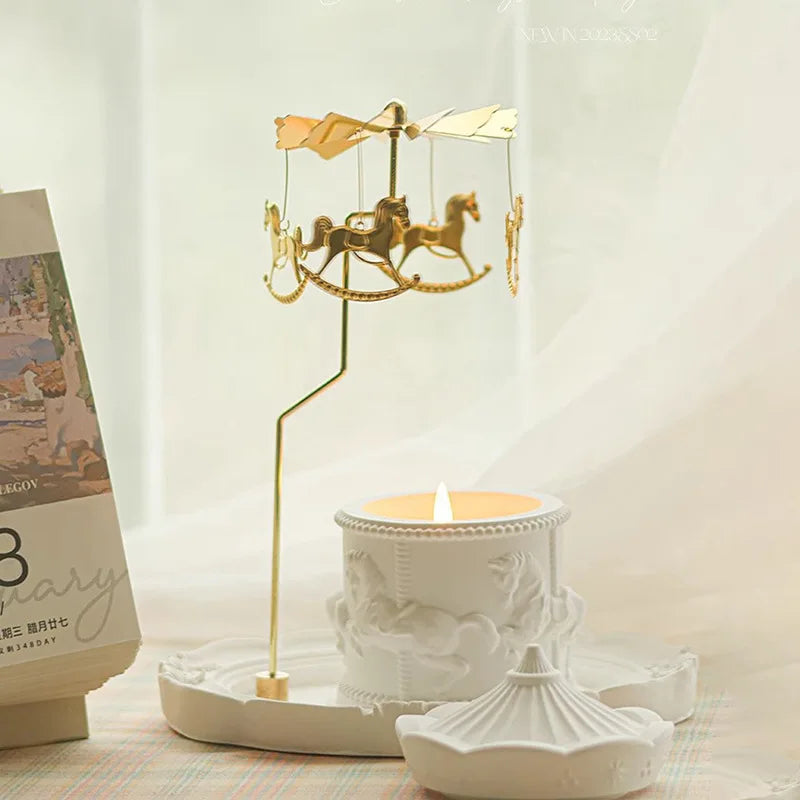Miniature carrousel doré avec des chevaux tournant sur un plateau blanc décoratif, à côté d'une bougie allumée sur un support en porcelaine blanche.