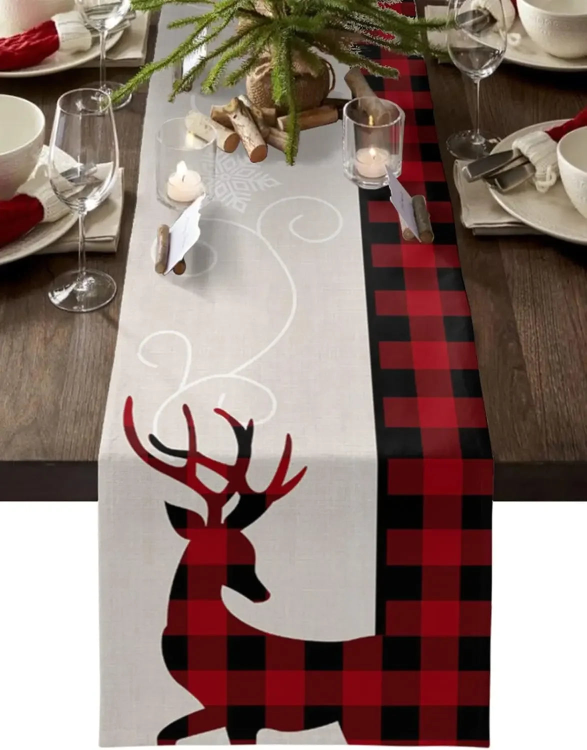 Une nappe de table blanche avec un motif de cerf rouge et noir, agrémentée de branches de sapin et de bougies, crée une ambiance chaleureuse et festive pour une table de Noël.