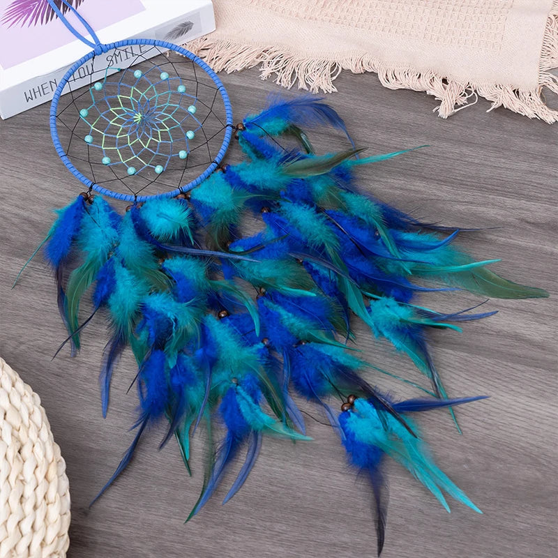 Un magnifique attrape-rêves artisanal aux plumes bleues et vertes, suspendu sur une surface en bois grisâtre avec des accessoires décoratifs.