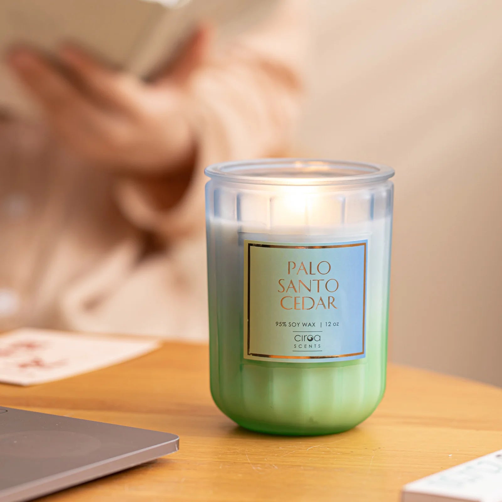 Une bougie parfumée Palo santo cedar dans un bocal en verre posée sur une surface en bois, avec un ordinateur portable en arrière-plan.