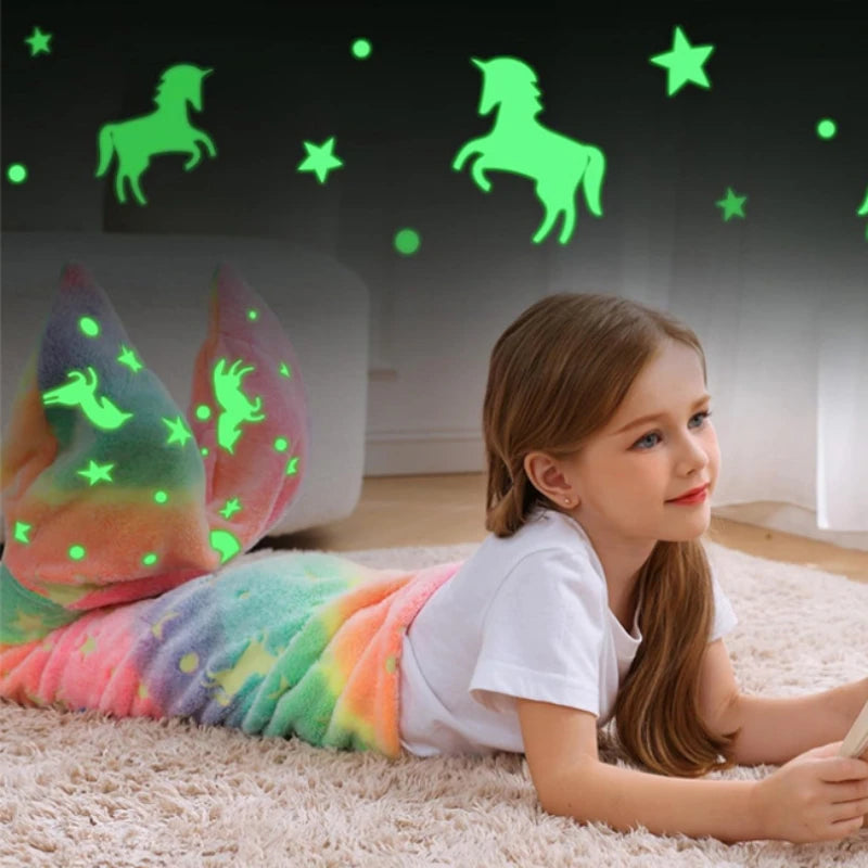 Jeune fille assise sur le sol devant un mur lumineux avec des licornes et des étoiles phosphorescentes.