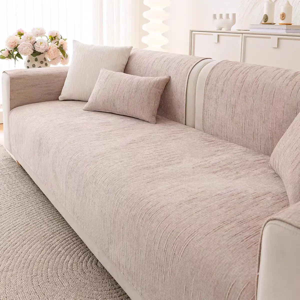 Ce salon confortable présente des coussins et un canapé en nuances de beige et gris, complétés par une touche florale et un meuble blanc, créant une atmosphère apaisante et élégante.