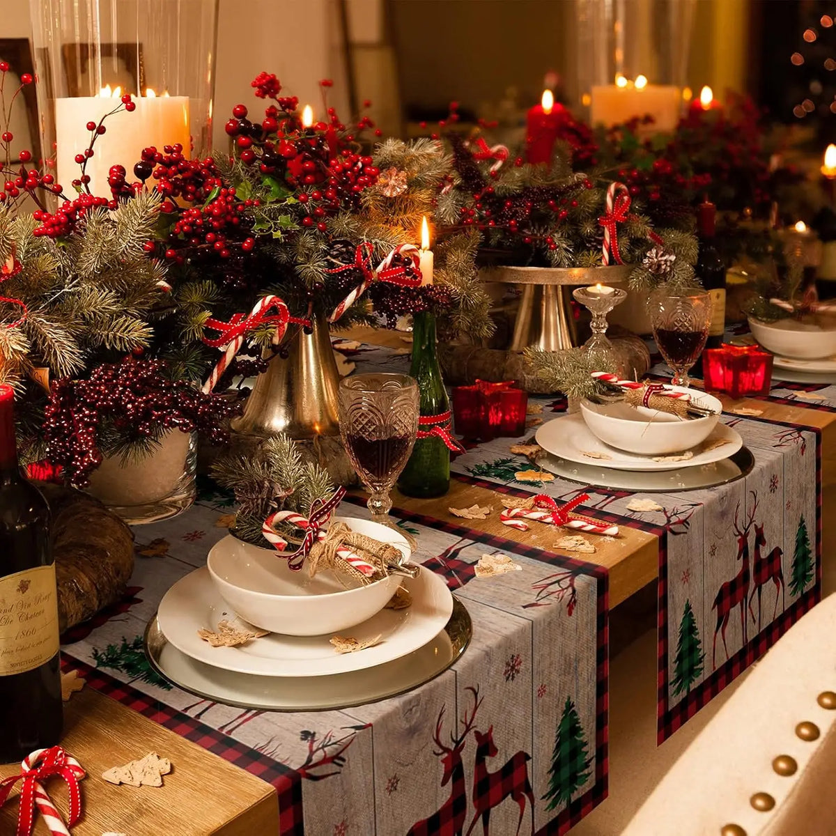 Une table de Noël joliment décorée avec des guirlandes de baies rouges, des bougies allumées et des plats de porcelaine blanche.