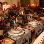 Une table de Noël joliment décorée avec des guirlandes de baies rouges, des bougies allumées et des plats de porcelaine blanche.