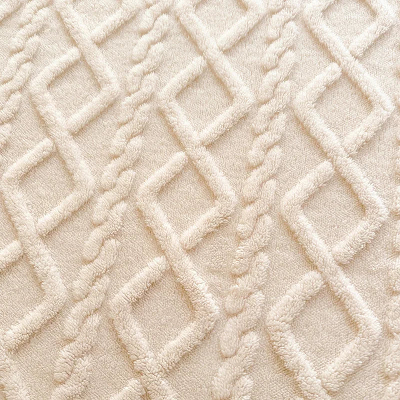 Cette image montre un gros plan d'un motif texturé de tissu moelleux de couleur beige clair, composé de motifs géométriques entrelacés.